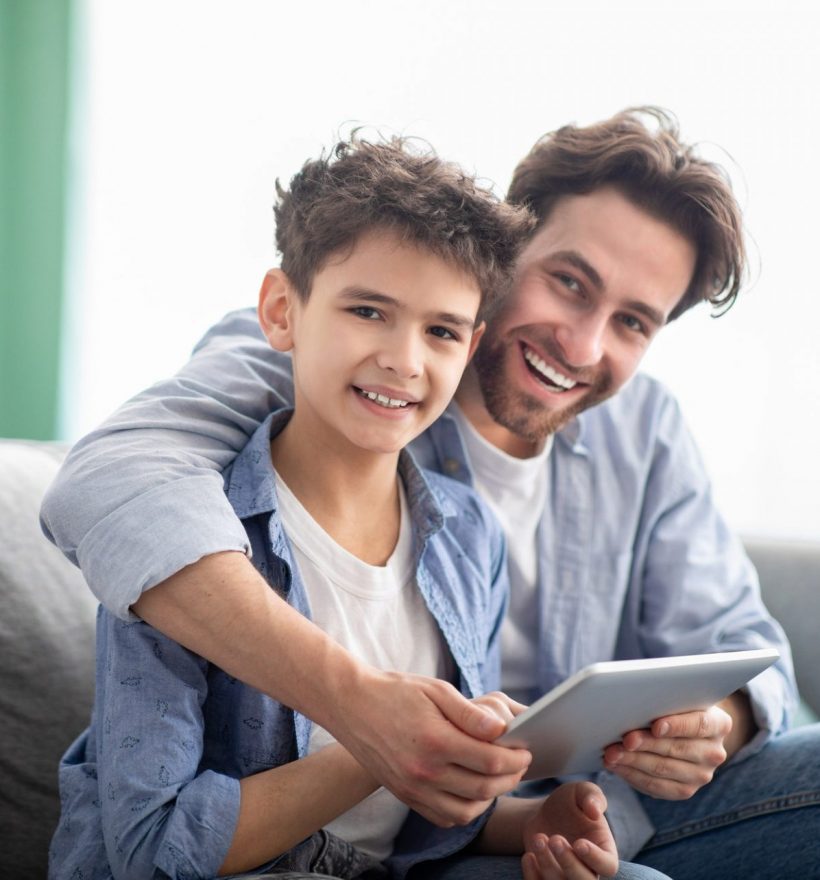 Family time. Happy dad and son using digital tablet, browsing internet online at home, sitting